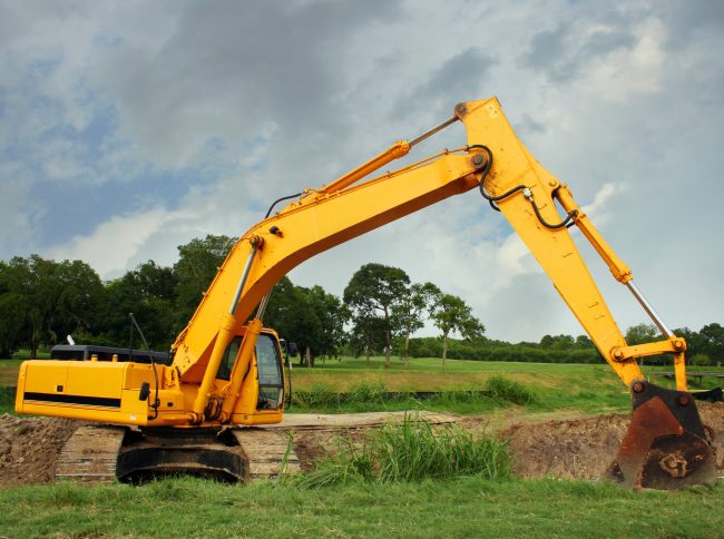 Yellow excavator digging on grassy field.