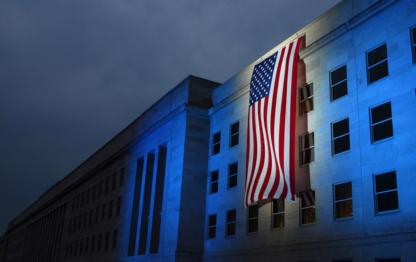A large american flag hanging from the side of a building.