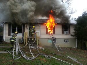 A house fire with two firemen on the front of it.