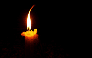 A candle is lit in the dark with its flame glowing.