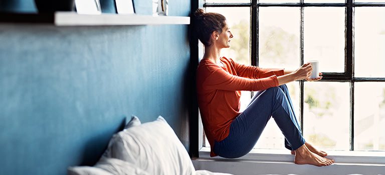 A woman sitting on the window sill of her bed.