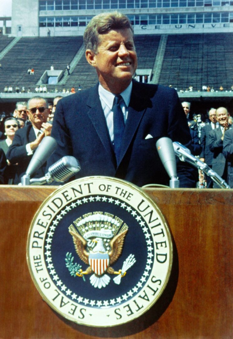 A man in suit and tie at podium with microphones.
