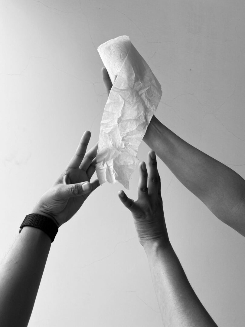 a hand holding a roll of toilet paper with two other hands reaching for it