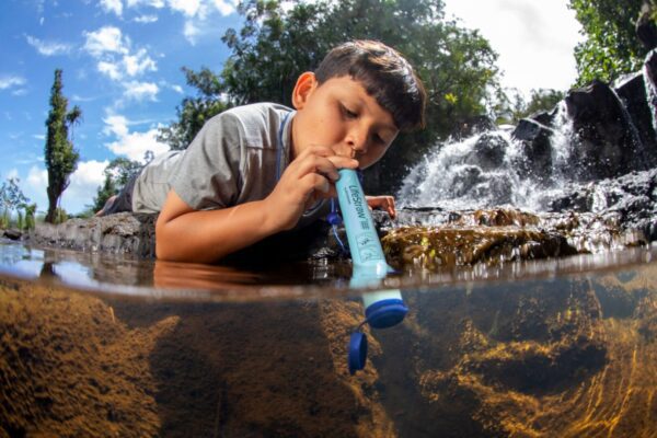 A boy is drinking water from the river