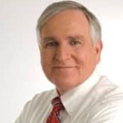 A man with gray hair wearing a white shirt and red tie.