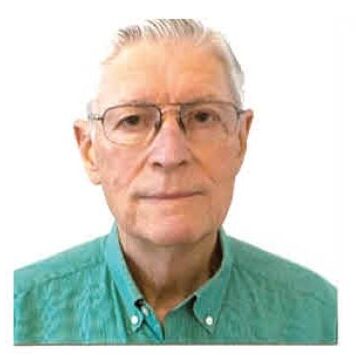 A man with glasses and white hair wearing a green shirt.