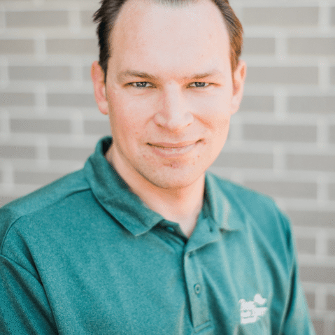 Man in a green polo shirt standing against a brick wall.