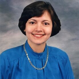 A woman in blue shirt and gold chain necklace.